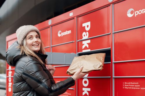 Smilende kvinne legger en pakke i Postens pakkeboks
