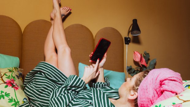 Kvinne ligger i sengen og ser på mobilen sin