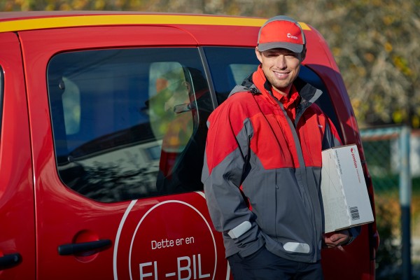 Mann med Posten-uniform som står foran en rød el-bil