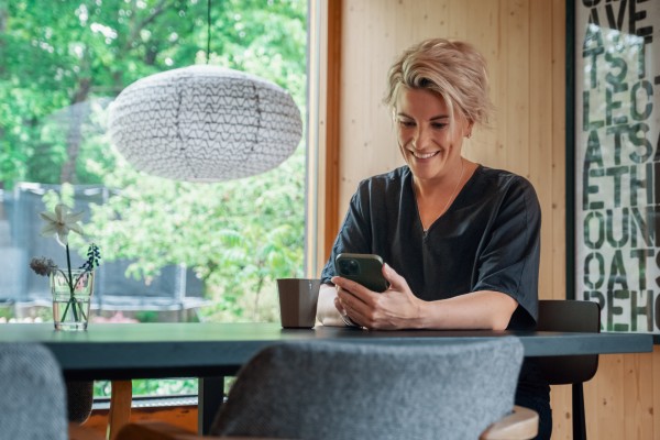 Kvinne sitter ved spisebord og ser på mobilen sin.
