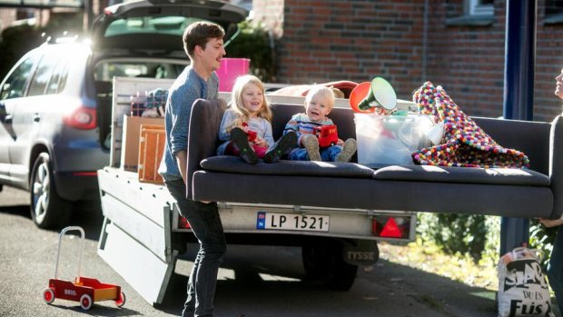 Et par bærer en sofa med to barn i fra en bilhenger.