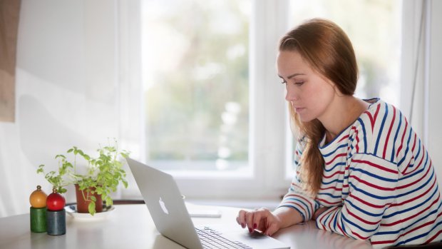 Kvinne med langt hår sitter foran en datamaskin hjemme