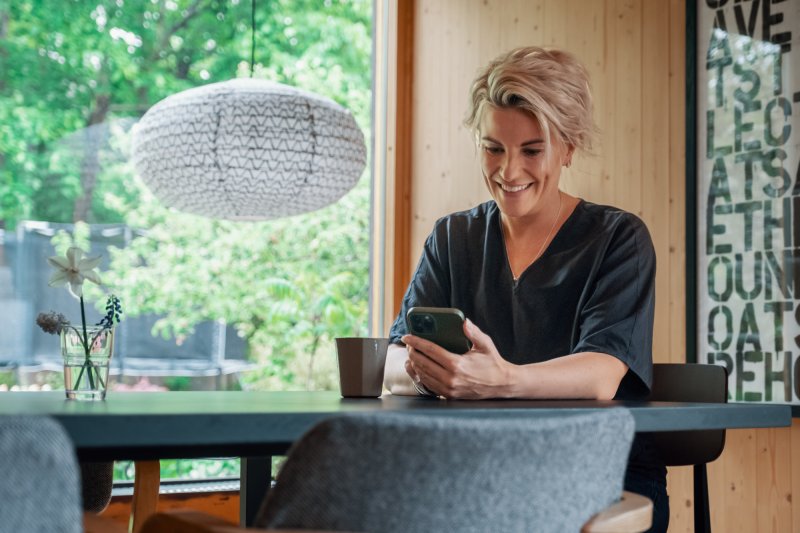 Smiling female customer with cellphone sitting by a dining table.