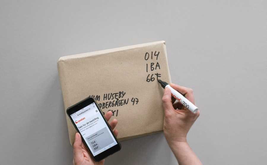 Writing the digital stamp code on a small package. The digital code showing on a phone.