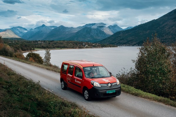 Elbil fra Posten på landevei foran norsk natur med fjell og vann