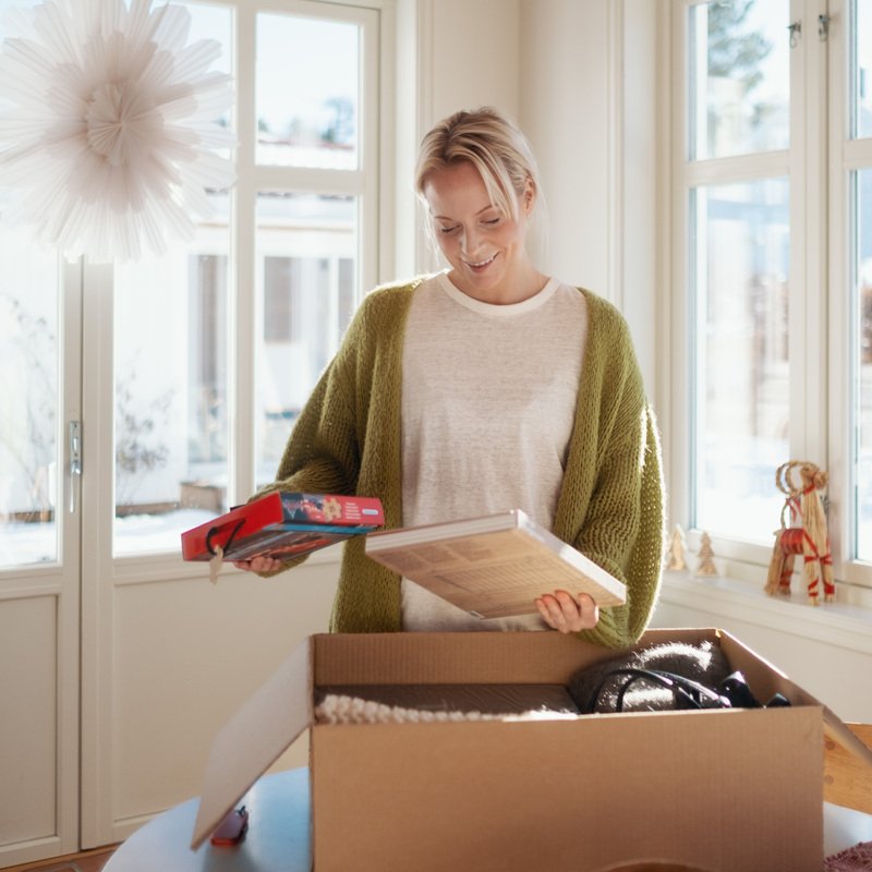 Kvinne i julepyntet hus, står med innhold fra en pappeske i hendene