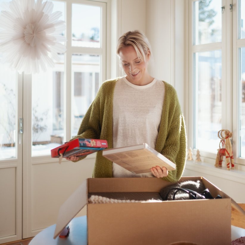 Kvinne i julepyntet hus, står med innhold fra en pappeske i hendene