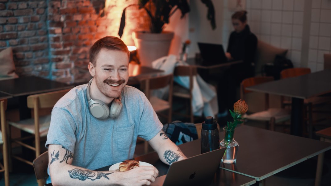 Ung mann smilende på kafe, med høretelefoner og pc