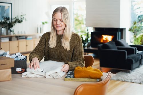 Kvinne sittende ved spisebord med esker og klær