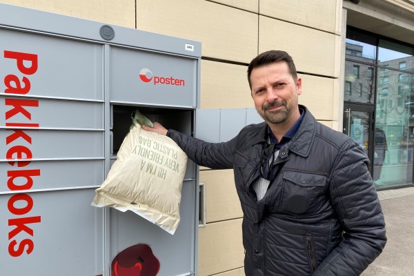 Mann som holder mobil og en pakke foran Postens Pakkeboks