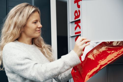 Kvinne med langt hår henter en pakke fra Postens Pakkeboks.