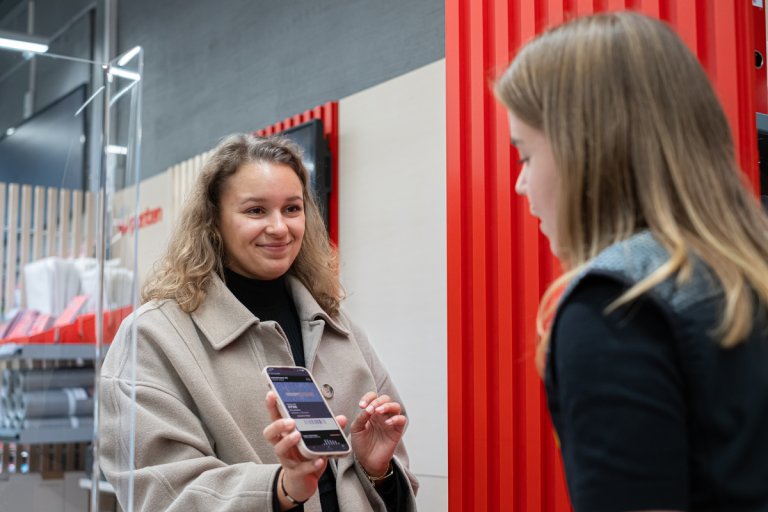 Kvinne på Posten viser mobilen til ansatt