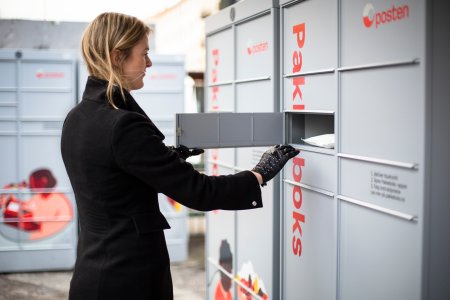 Kvinne foran åpen luke i en pakkeboks fra Posten.