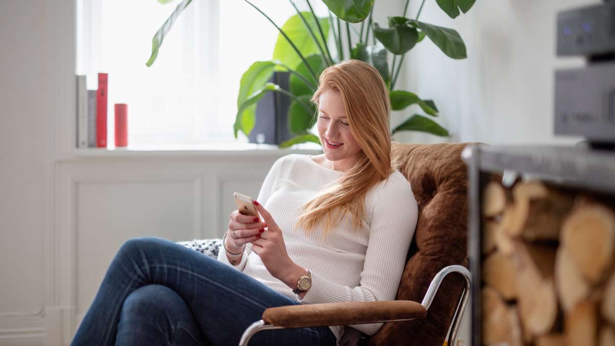 Kvinne sitter i lenestol og ser på mobilen sin