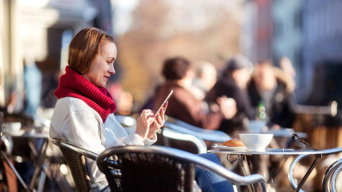 Kvinne på utekafe ser på mobilen sin