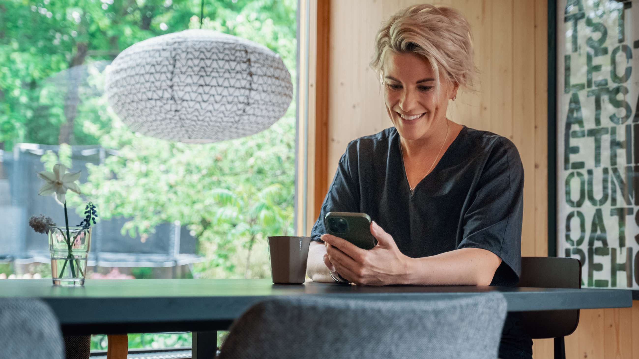 Kvinne sitter ved spisebord og ser på mobilen sin.
