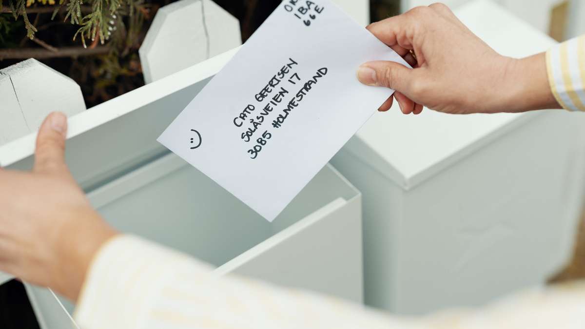 Konvolutt med adresse og digitalt frimerke puttes oppi en postkasse