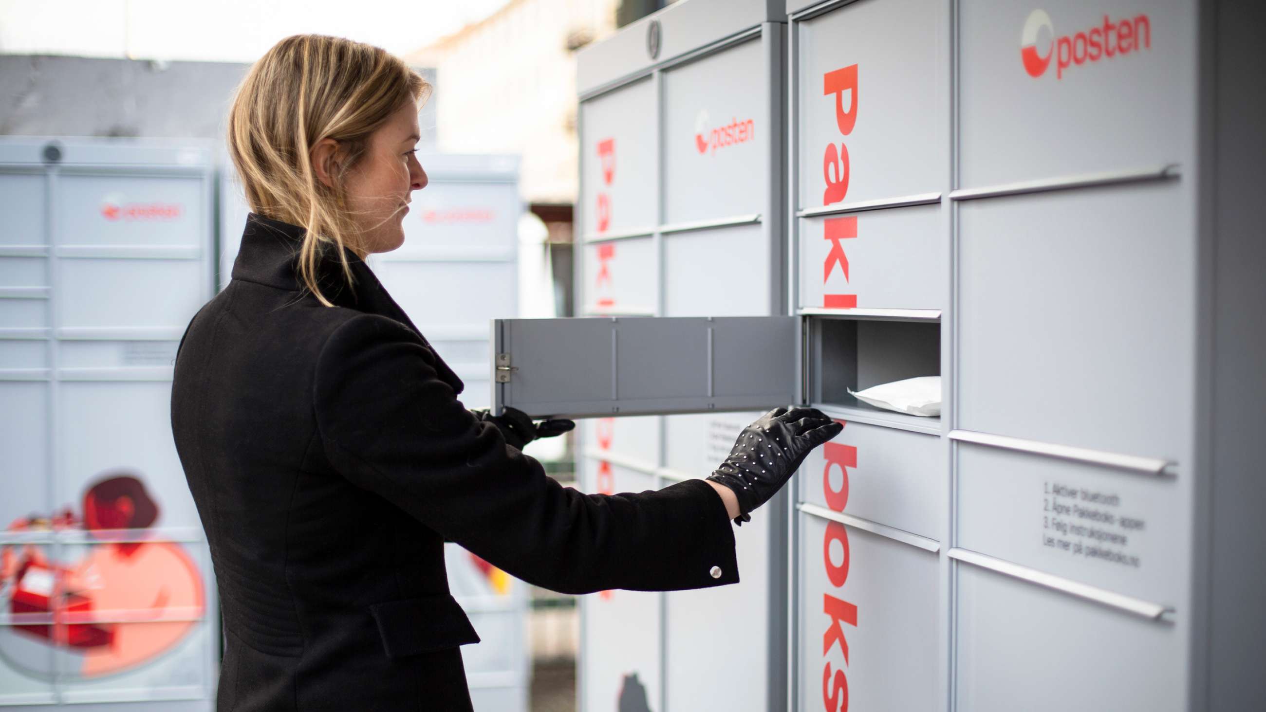 Kvinne foran åpen luke i en pakkeboks fra Posten.