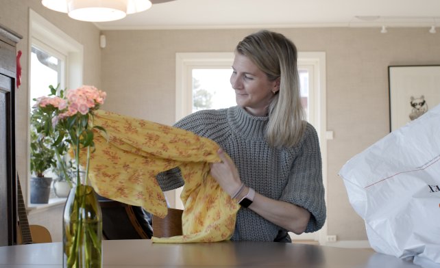 Kvinne som bretter sammen en gul kjole. På bordet foran seg har hun blomster og en Fretex-pose.