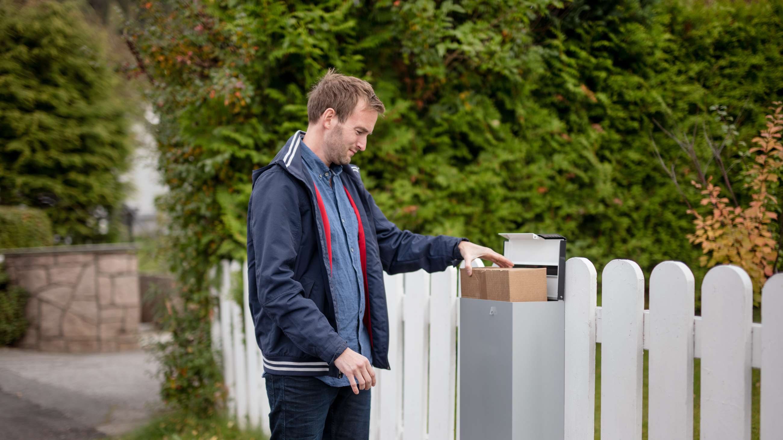 Mann som putter en pakke ned i en grå postkasse.