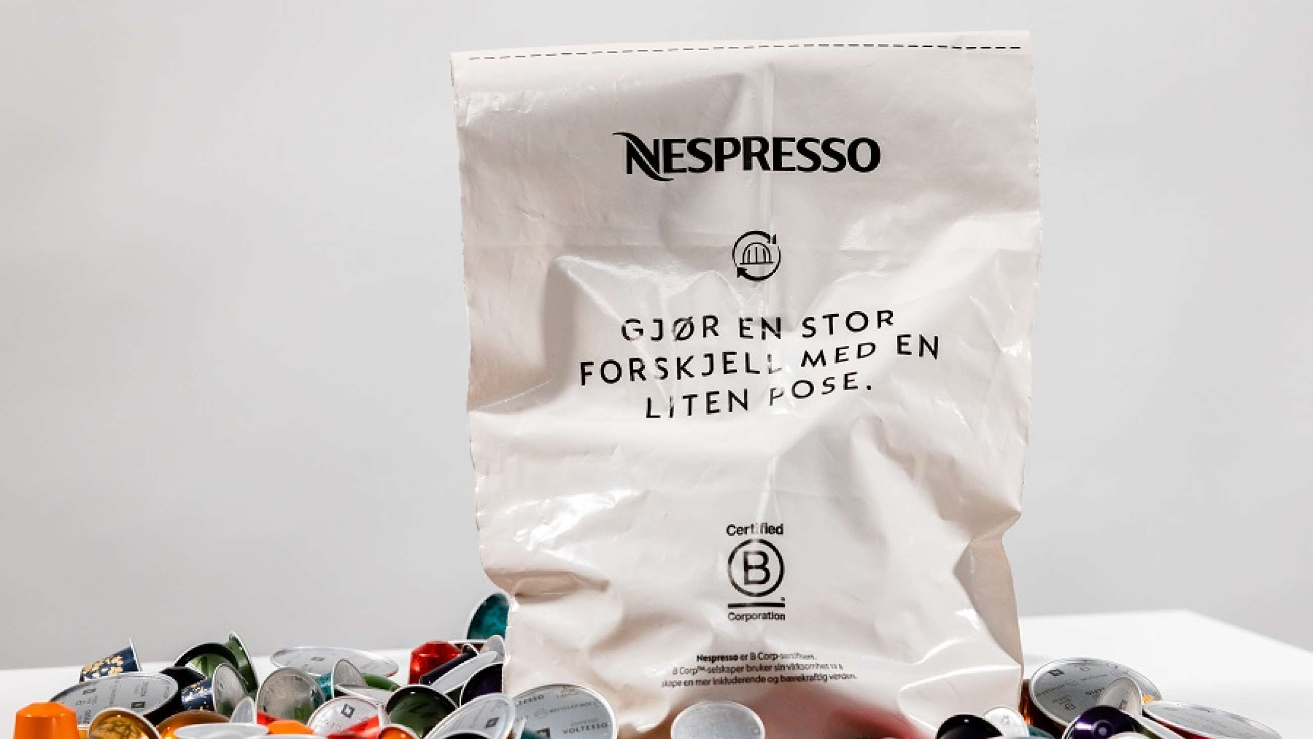 Gjenvinningspose fra Nespresso på bord sammen med mange kaffekapsler