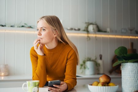 Kvinne i tenkende positur på et kjøkken, med mobil i hånden