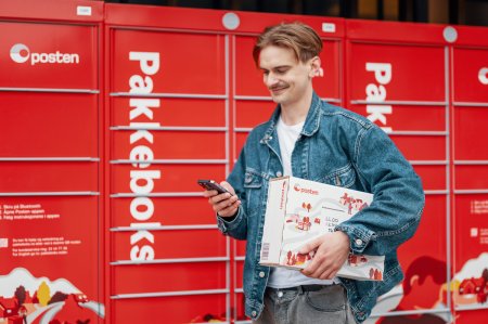 Smilende mann med en pakke foran Postens pakkeboks