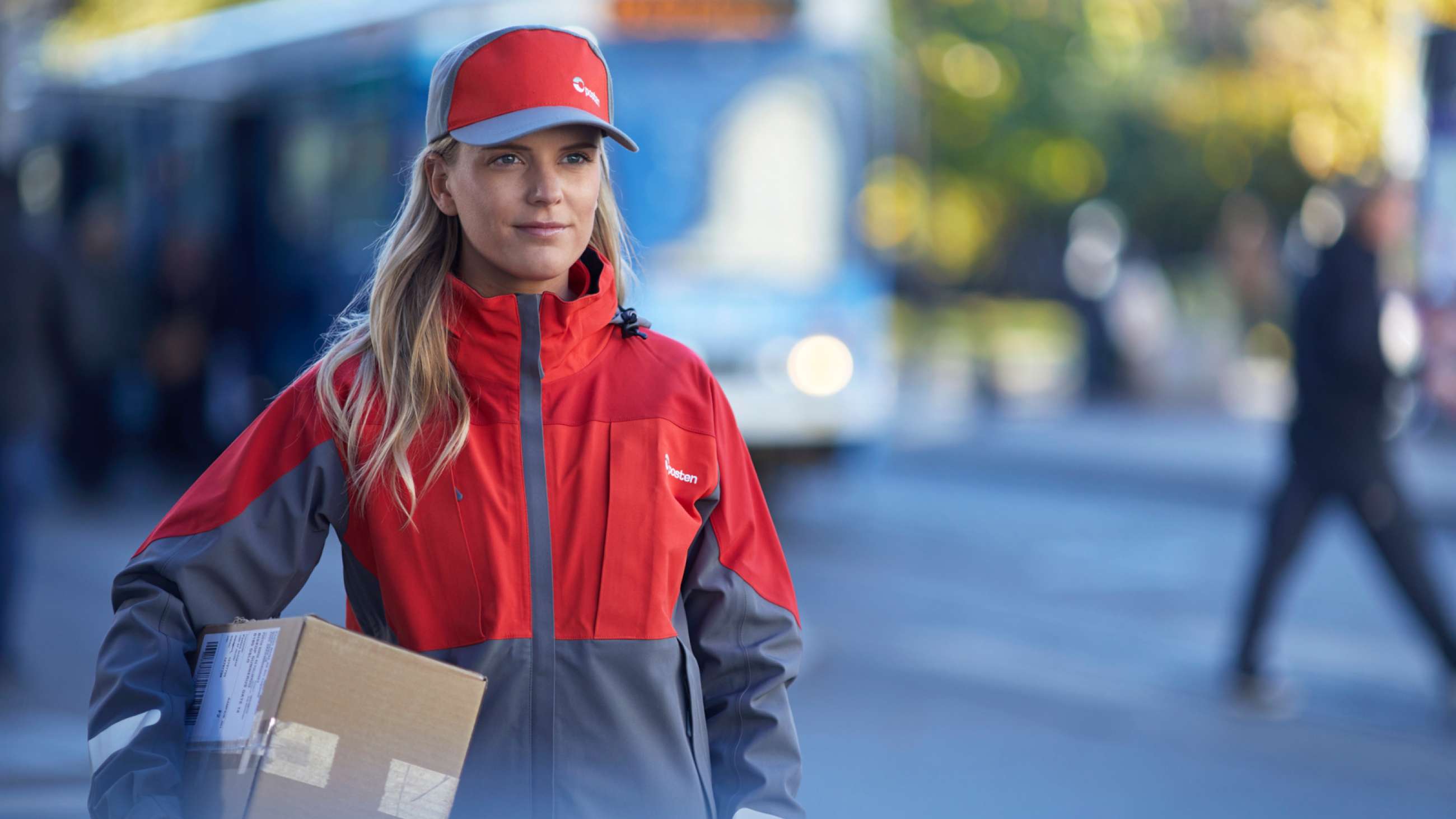Kvinnelig postbud med pakke under armen i urbant strøk