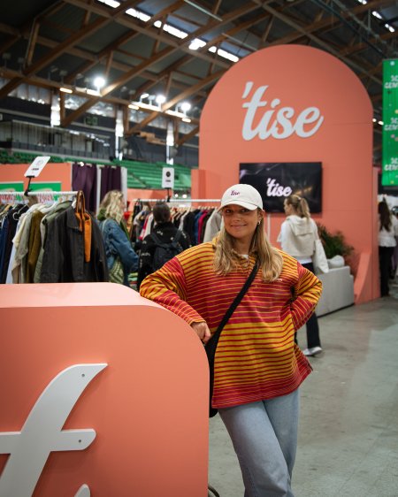Kvinne med caps og stripete genser, poserer foran et Tise-skilt