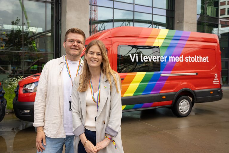 Mann og kvinne poserer foran regnbue-dekorert postbil