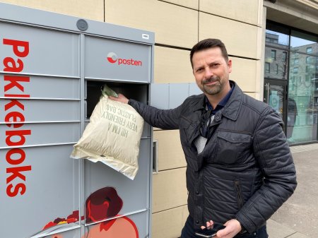 Mann som holder mobil og en pakke foran Postens Pakkeboks