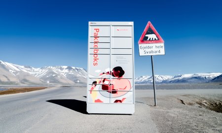 Postens Pakkeboks plassert ut i Svalbard, omgitt av fjell og ved siden av et fareskilt med isbjørn.