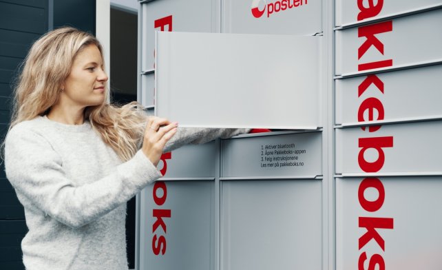 Kvinne med langt hår henter en pakke fra Postens Pakkeboks.
