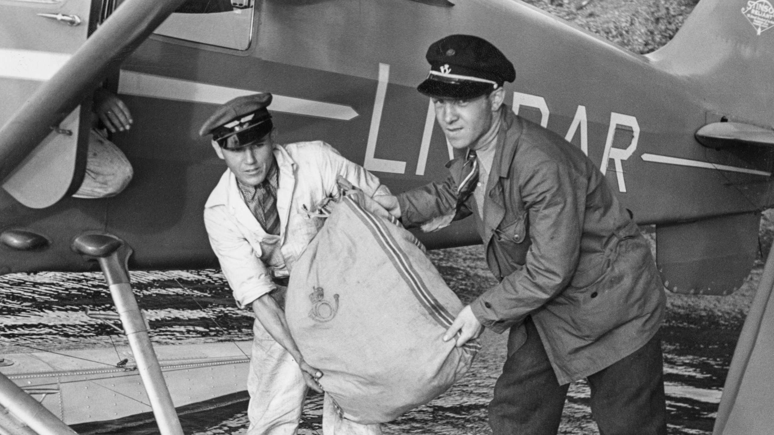 Postfrakt med sjøfly i 1936. To menn lemper tung postsekk ombord.