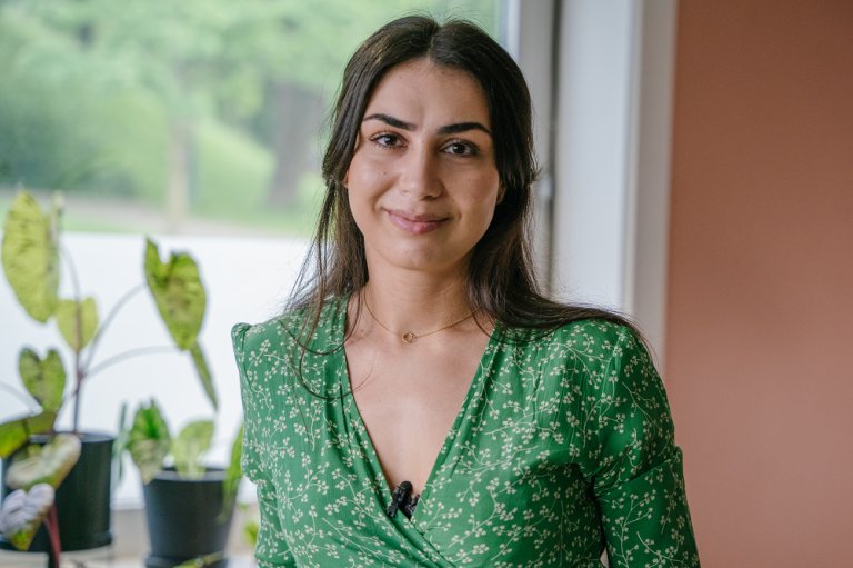 Ung kvinne med grønn kjole fotografert foran et vindu med planter.