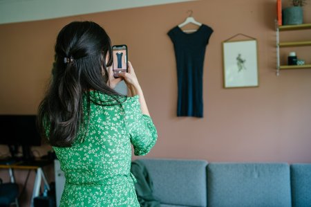 Kvinne i grønn kjole med ryggen til kameraet. Tar bilder av en kjole med mobilen.