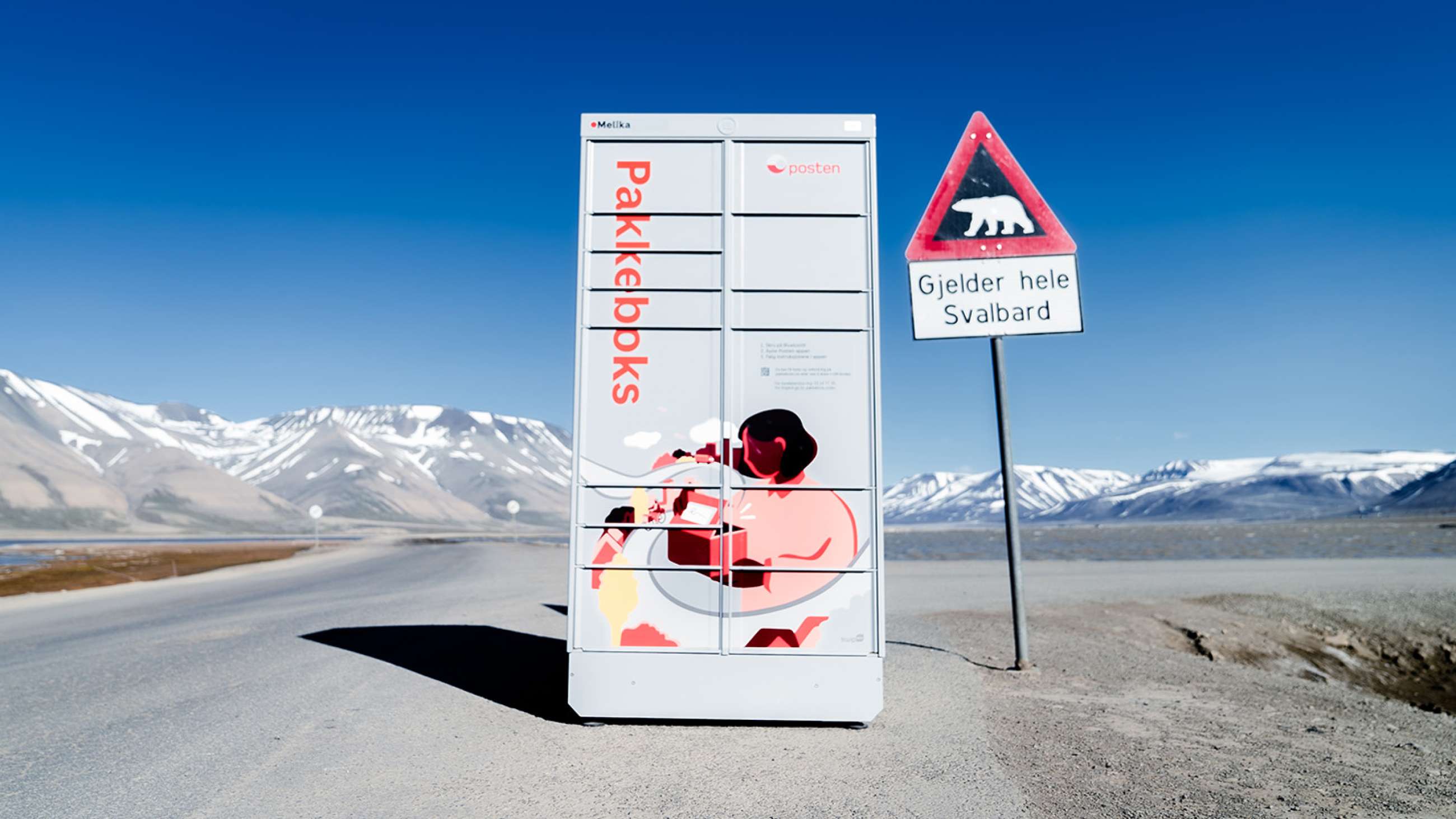 Postens Pakkeboks plassert ut i Svalbard, omgitt av fjell og ved siden av et fareskilt med isbjørn.