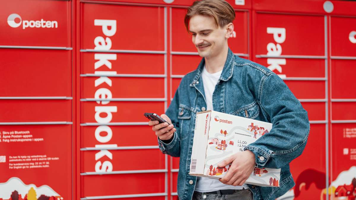 Smilende mann med en pakke foran Postens pakkeboks