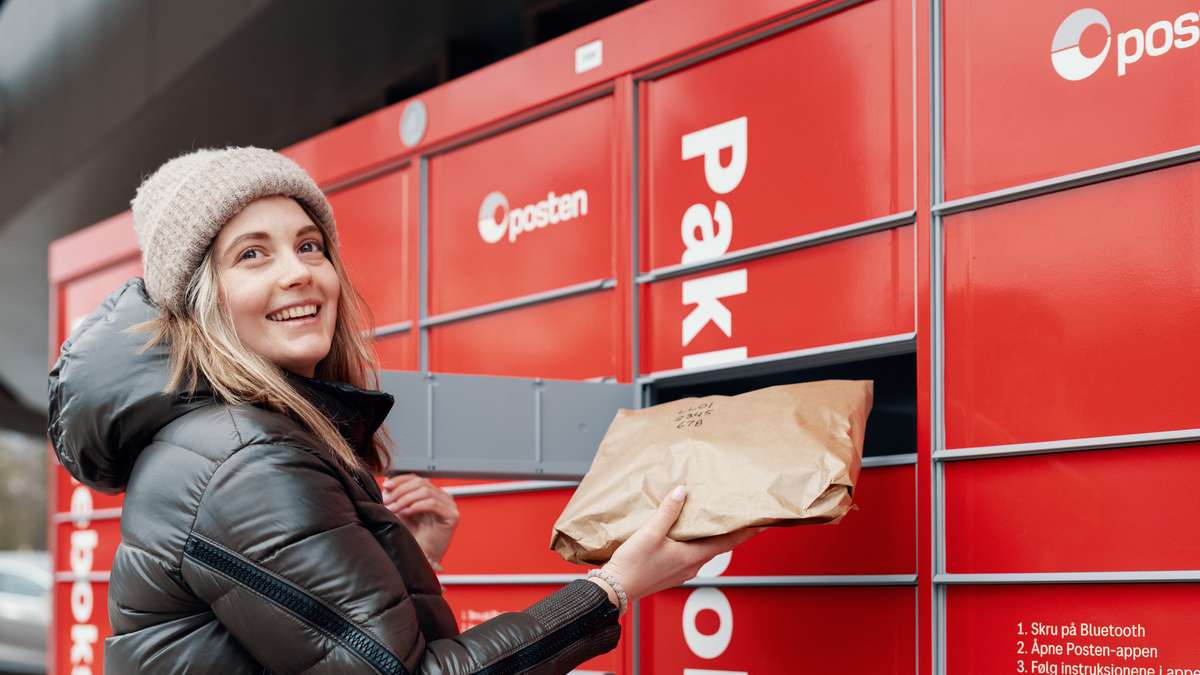 Smilende kvinne legger en pakke i Postens pakkeboks