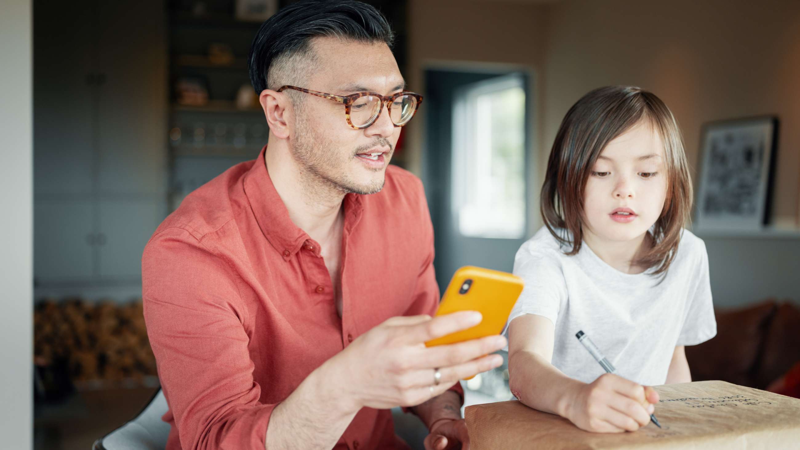 Far med mobiltelefon og datter som skriver sendekode på en pakke