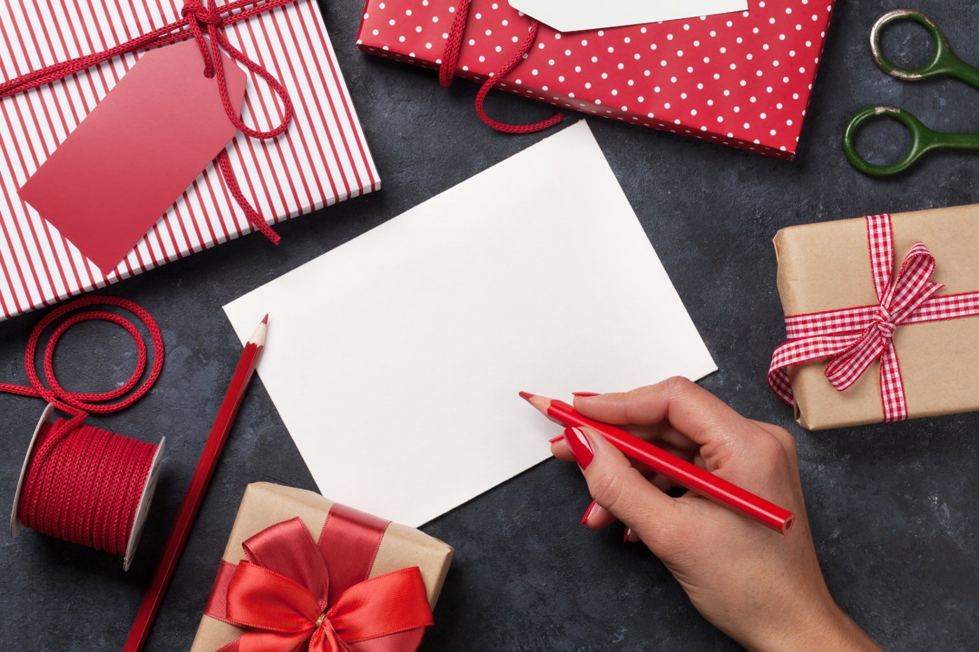 Kvinne skriver julekort og pakker julegaver på svart bordplate