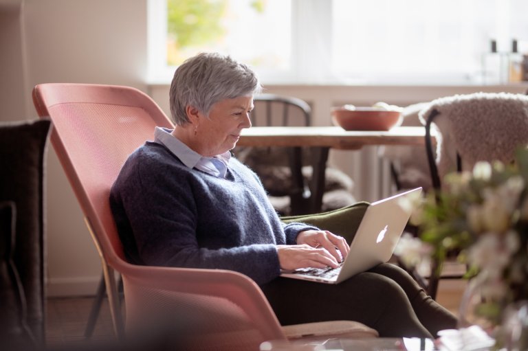 Eldre dame sitter i en rosa stol med en laptop på fanget