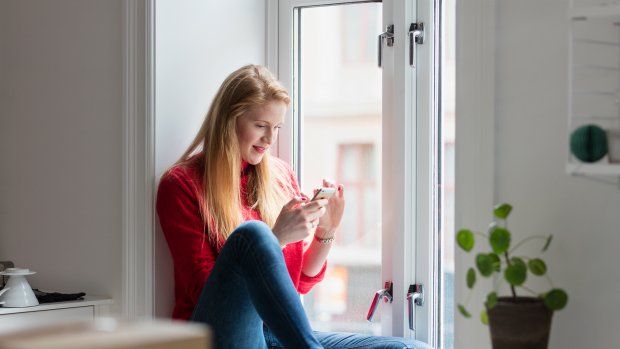 Kvinne sitter i vinduskarm med smarttelefon i hånden