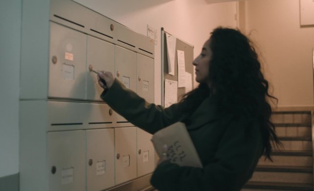 Dame med langt hår åpner postkasse i et postkasseanlegg i en bygård
