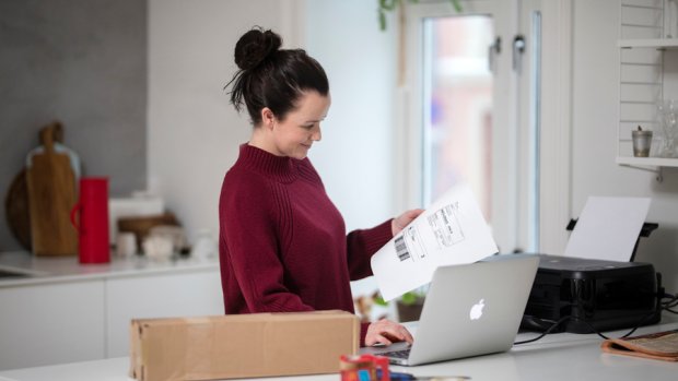 Dame med utskrift av adresselapp med tollinformasjon i hånda; og datamaskin og en printer på benken