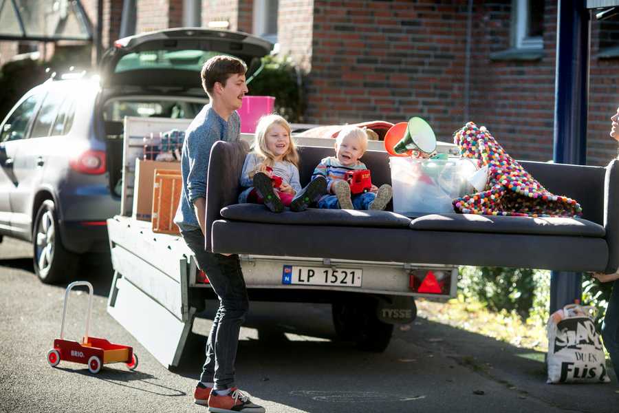 A couple is holding a sofa with two kids and home stuff on the pavement