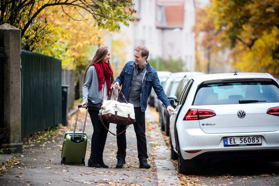 A couple with a suitcase and a bag outside a car